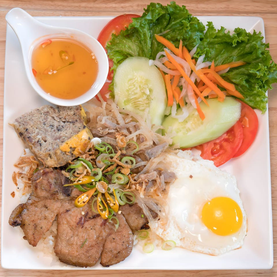 Vietnamese broken rice dish with grilled pork, fried egg, meatloaf, and fresh vegetables.