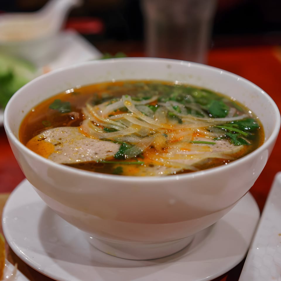 Close-up of a bowl of Vietnamese pho with broth, noodles, meat, and herbs.