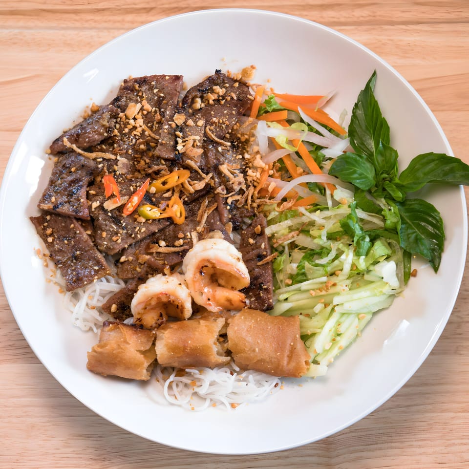 Vietnamese vermicelli bowl with grilled beef, shrimp, spring rolls, and fresh vegetables.