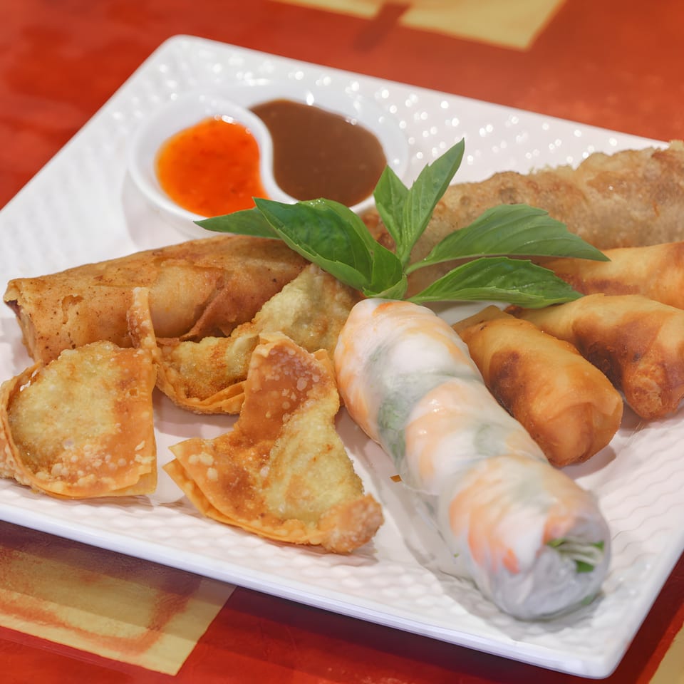 A platter of Vietnamese appetizers including spring rolls, fried wontons, and a fresh shrimp roll.
