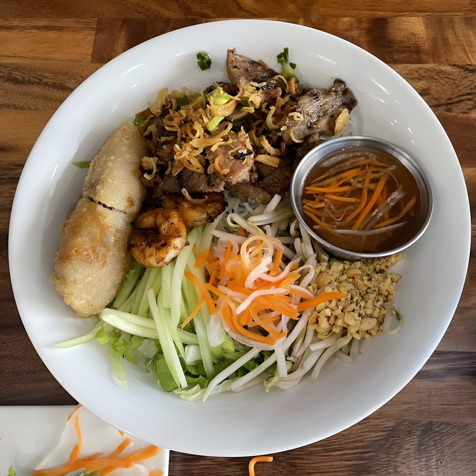 A Vietnamese vermicelli bowl with grilled meat, shrimp, egg roll, and vegetables.