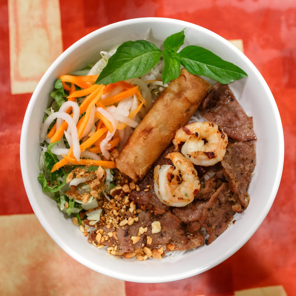 Pho Nom Nom's vermicelli bowl with grilled beef, shrimp, egg roll, and fresh vegetables.