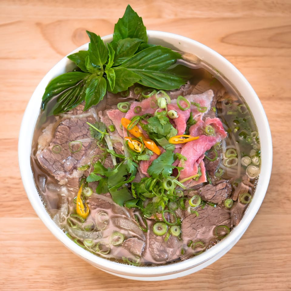 A bowl of Pho Nom Nom Vietnamese pho with beef, noodles, basil, cilantro, and chili peppers.